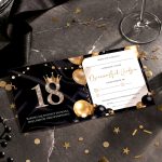 Elegant black and gold birthday invitation for an 18th birthday with a crown and gold balloons on a dark surface.