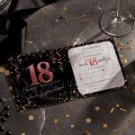 Opened birthday invitation with pink glitter '18' on black left panel and RSVP form on the right, surrounded by gold confetti and a wine glass base visible on a marble surface.